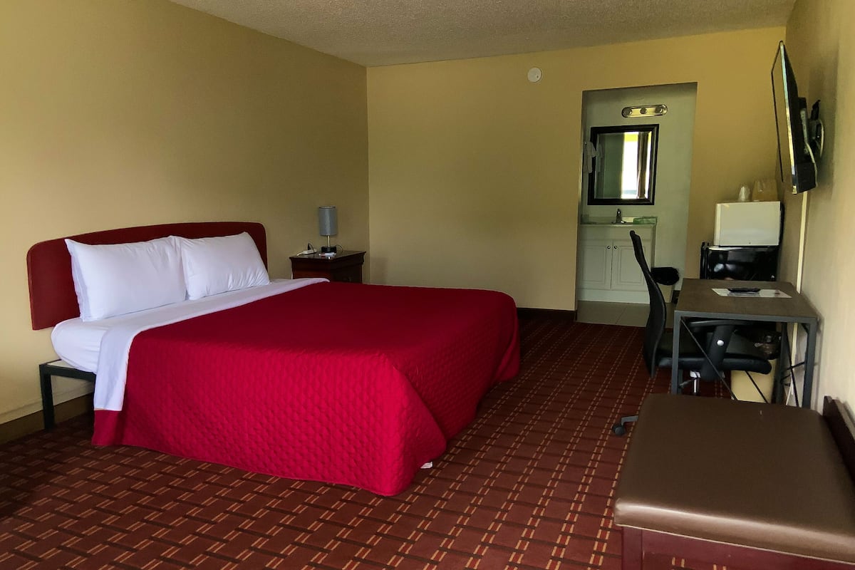A hotel room with a bed, a desk, a chair, a TV, and a small kitchenette.