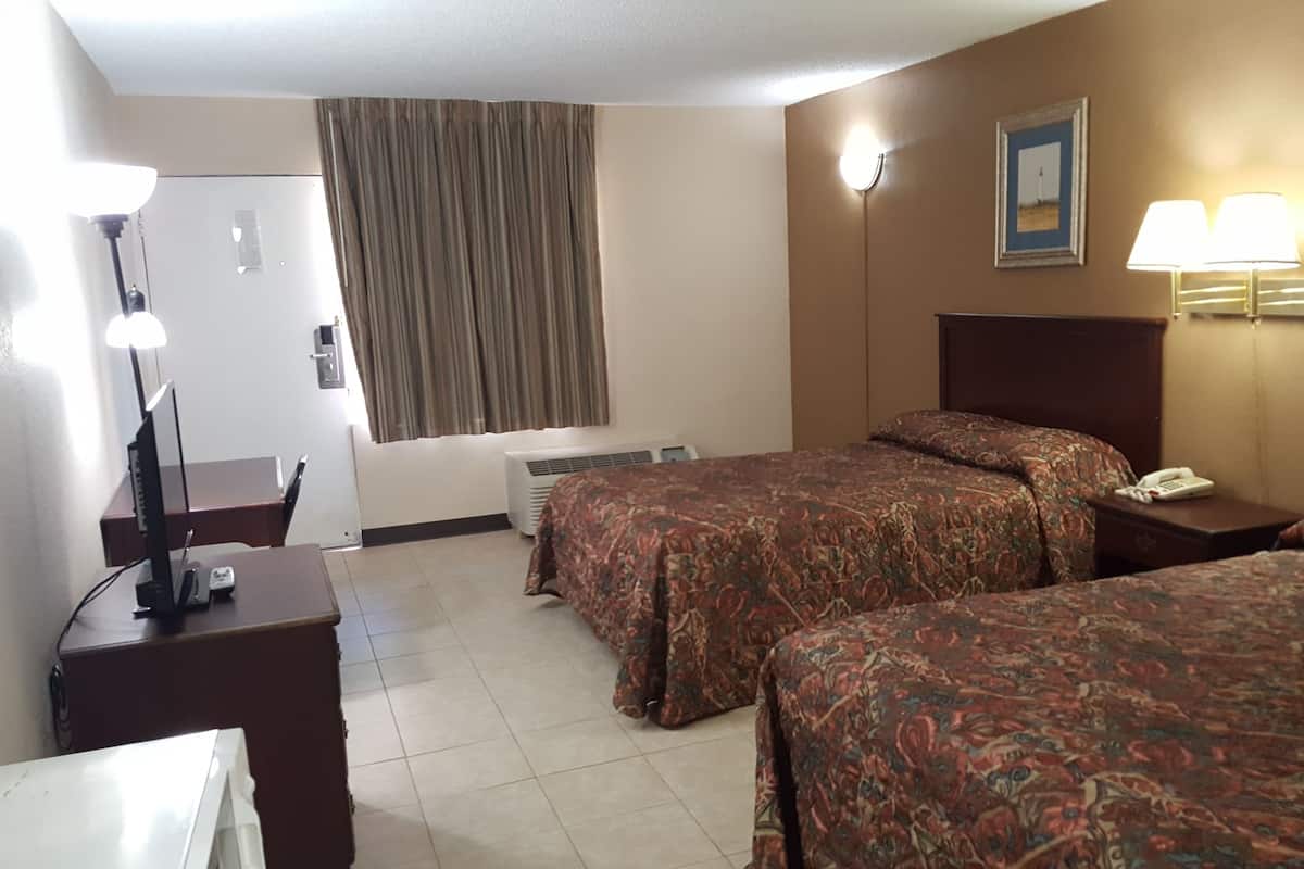A hotel room with two beds, a desk with a lamp, a telephone, and a picture on the wall.