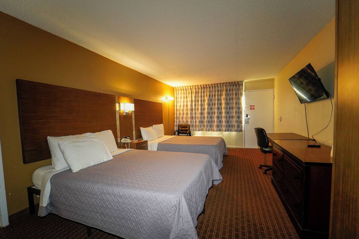 A hotel room with two beds, a desk, a chair, a TV, and a window with curtains.