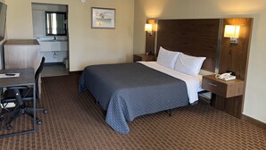 Ein Hotelzimmer mit Bett, Schreibtisch, Stuhl, Nachttisch, Lampe und einem Gemälde an der Wand.