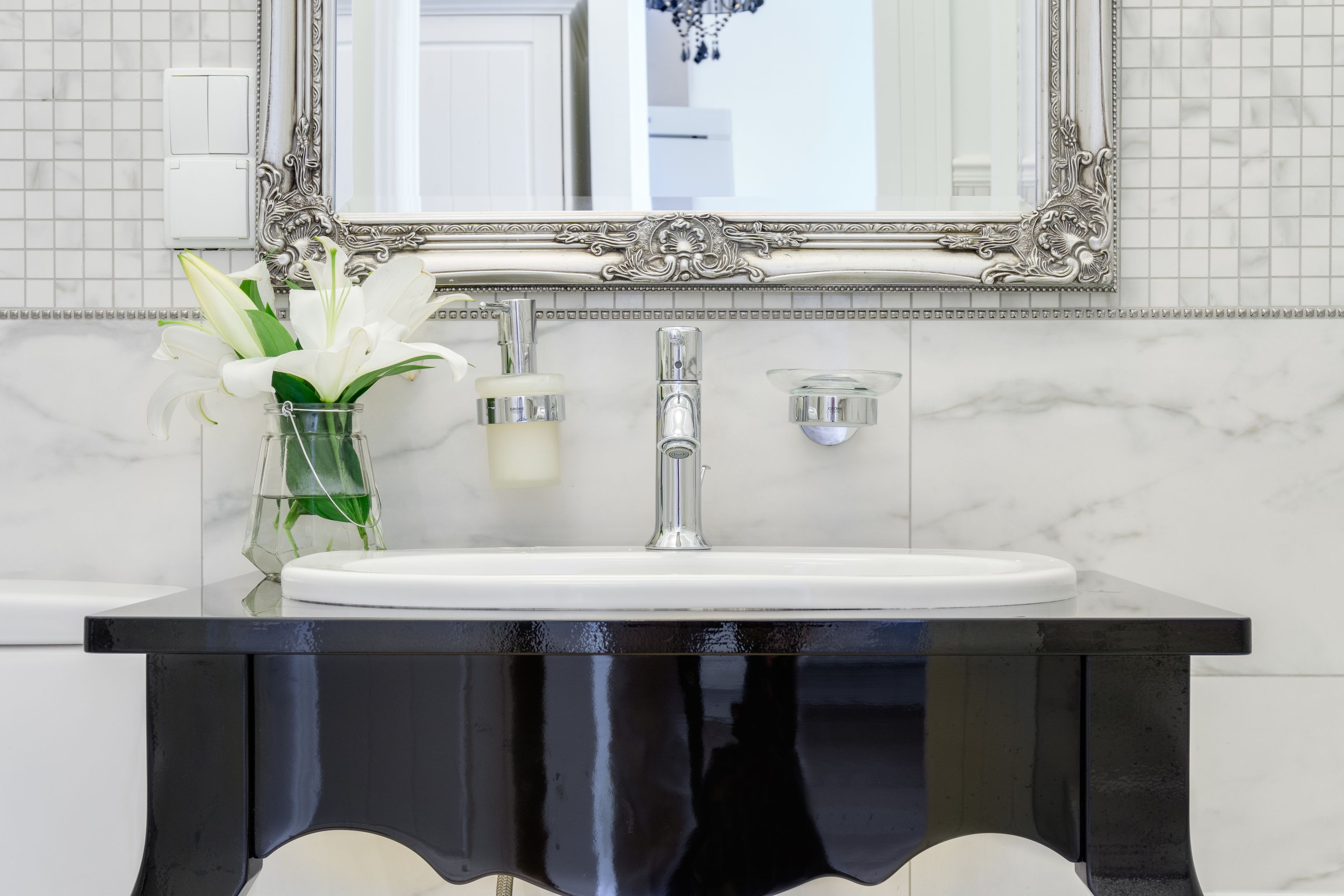 A bathroom with a black vanity, a white sink, and a large ornate mirror.