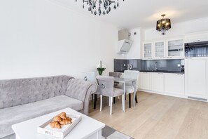 A modern living room with a grey sofa, a dining table with chairs, and a kitchen area with white cabinets and a black countertop. - Elite Apartments Browar Deluxe (Gdansk)