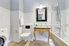 A modern bathroom with a glass-enclosed shower, a white toilet, a washing machine, and a wooden vanity with a sink.