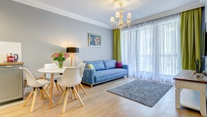 A modern living room with a sofa, dining table, chairs, a chandelier, and a kitchen area.