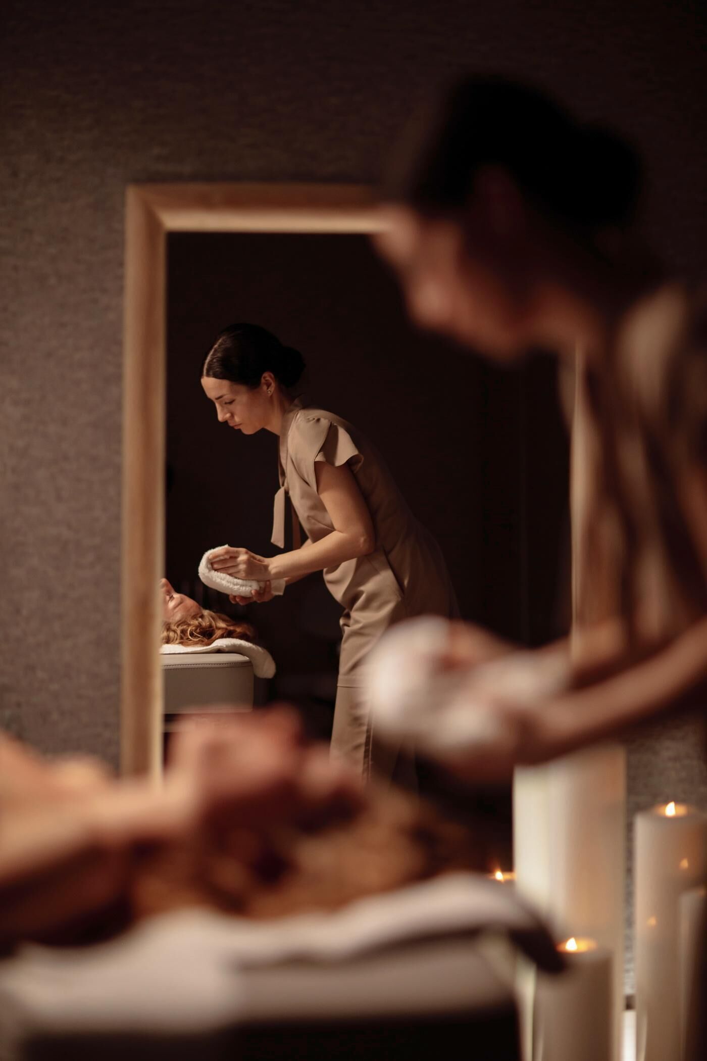 A spa room with a massage table, candles, and a person attending to a client.