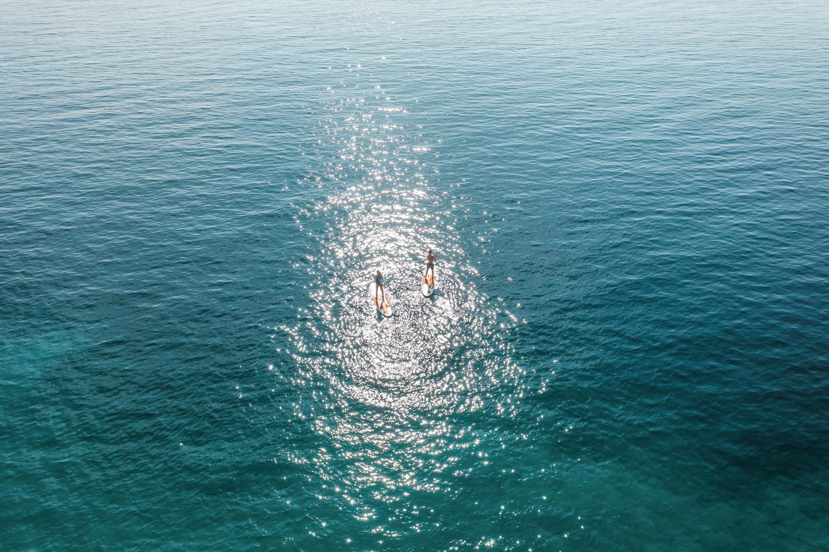 An aerial view of a calm sea with two boats creating a circular pattern on the water.