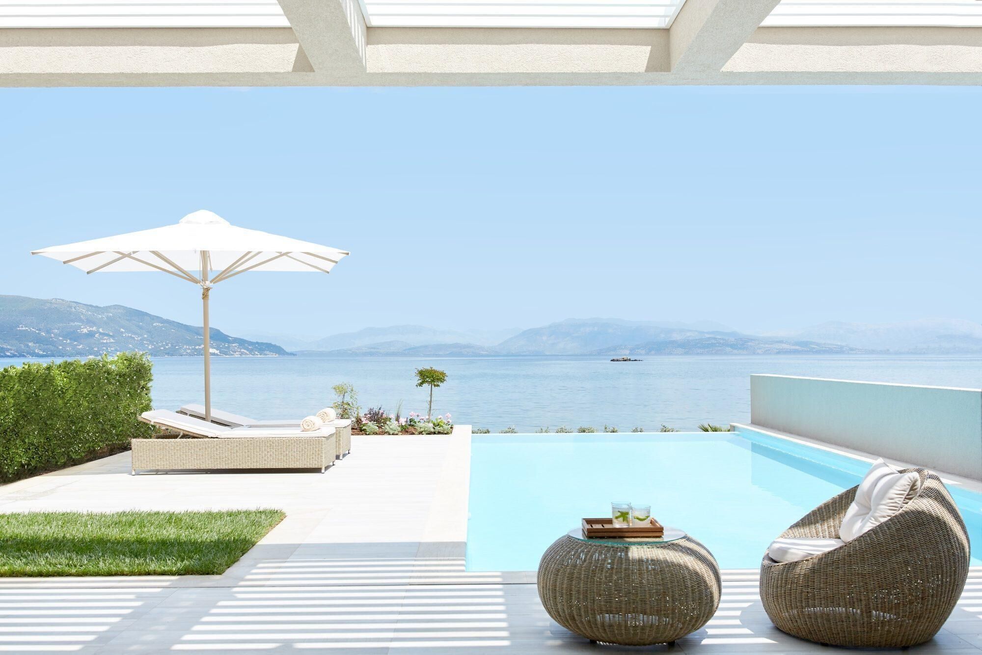 Ein Poolbereich mit Meerblick, eine Liege, Sonnenschirm und ein kleiner Tisch mit Getränken.