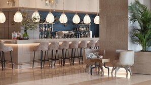 A modern bar area with a long counter, multiple bar stools, and hanging pendant lights.