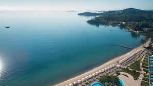 Vista aérea de un complejo turístico costero con playa, piscina y muelle.