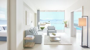 Una sala moderna con sofá, sillón y mesa de centro, un ventanal con vista al mar y una lámpara.
