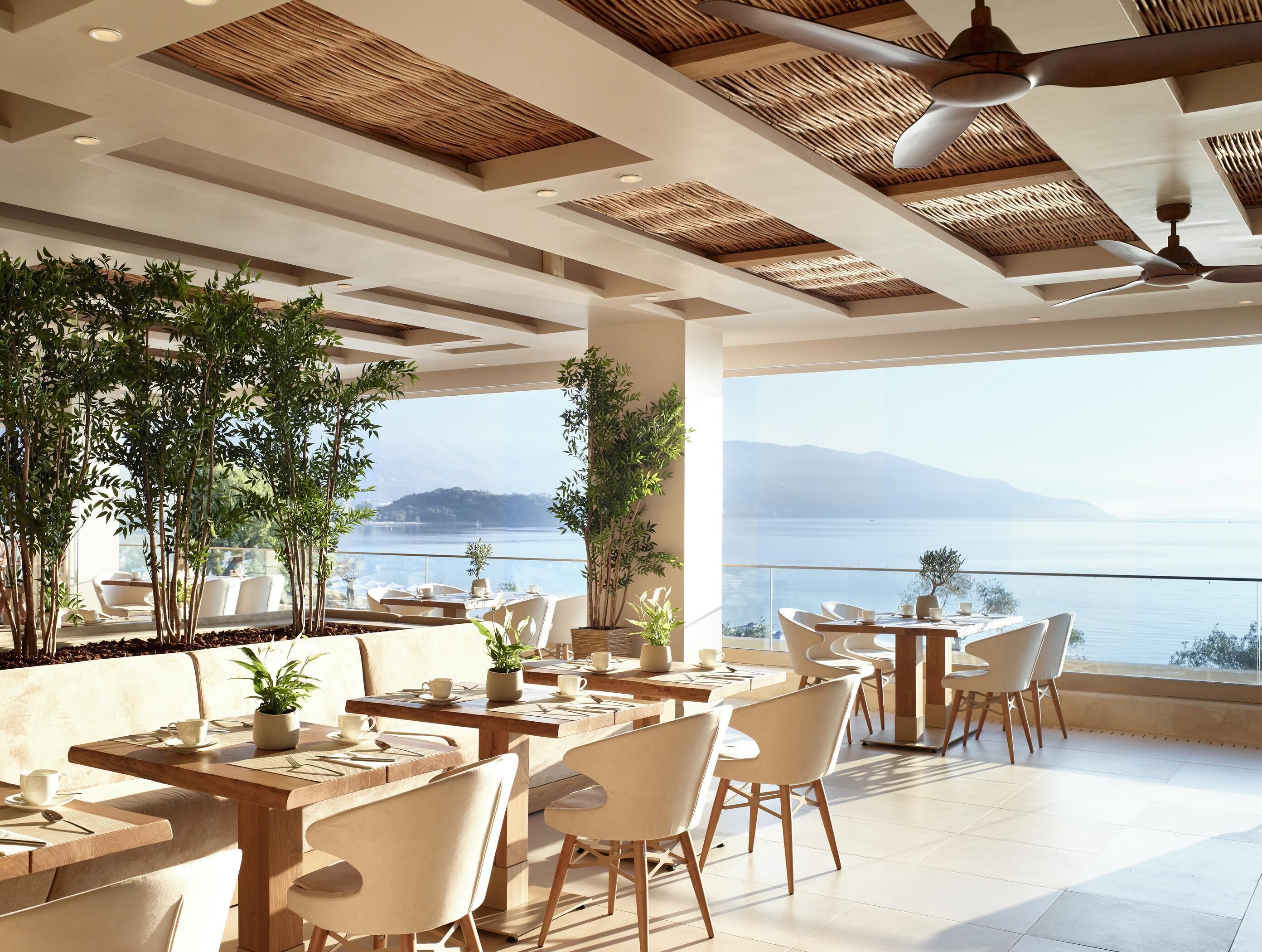 Un ristorante con tavoli e sedie, ampie finestre e piante in vaso.