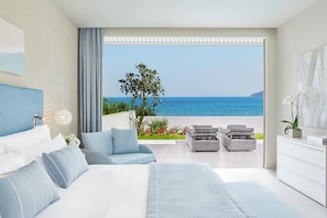Un dormitorio moderno con una cama grande, un área de descanso con vista al mar y un balcón con mobiliario exterior.