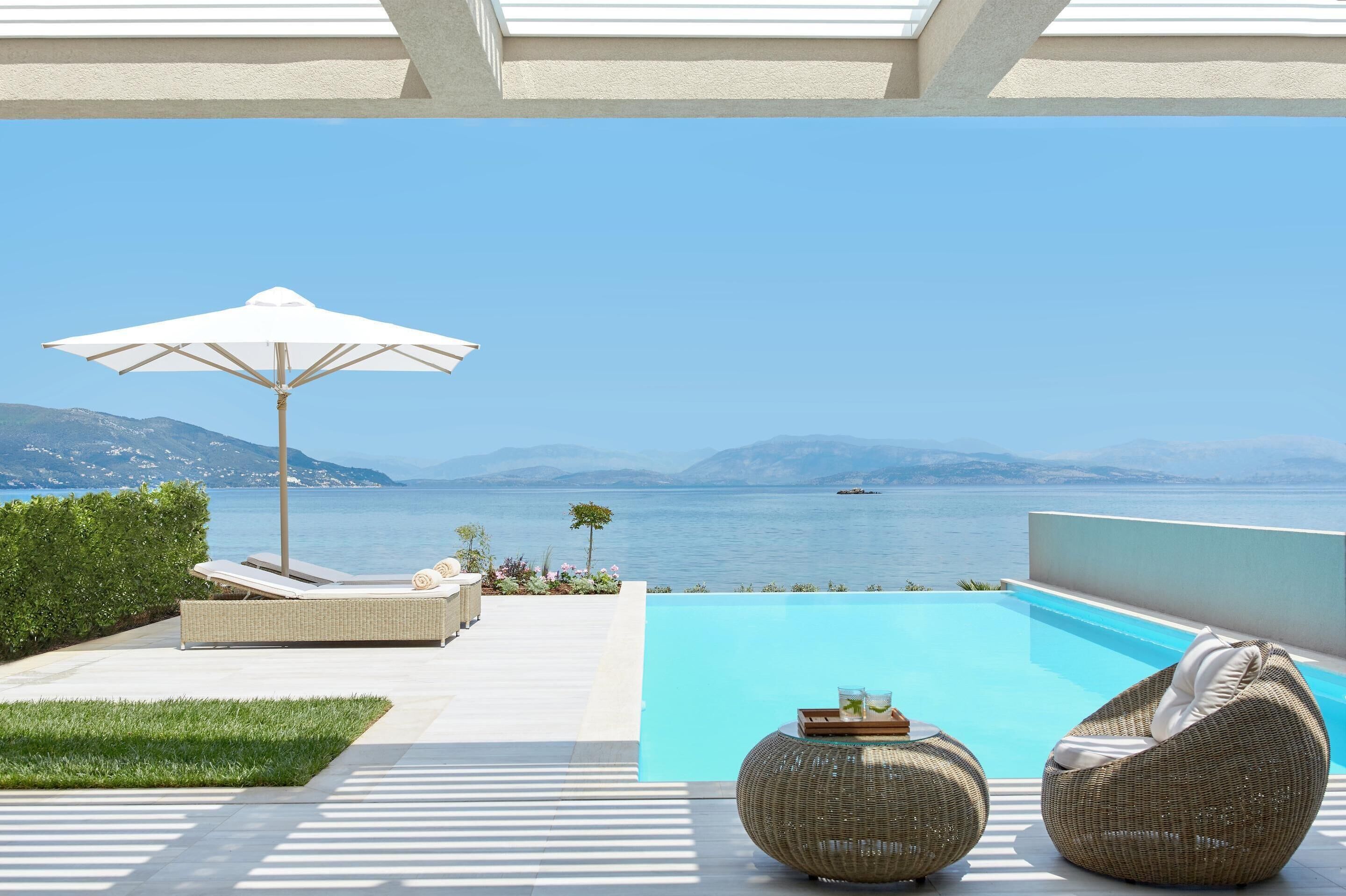Ein Poolbereich mit Liegestühlen und Sonnenschirm, mit Blick auf ein Gewässer und entfernte Berge.