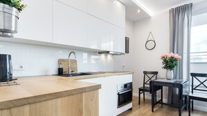 Een moderne keuken met witte kasten, een houten aanrecht, een inbouwoven en een eethoek met een tafel en stoelen.