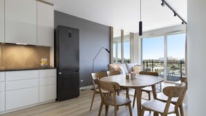 Een moderne keuken met witte kastjes, een zwarte koelkast en een eethoek met houten stoelen en een ronde tafel.