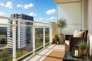 A balcony with a wicker sofa, a potted plant, and a candle on a table. - Elite Apartments Marine Cztery Oceany (Gdansk)