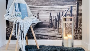 A cozy room with a beach-themed mural, a small seating area with a book, and a candle. - Elite Apartments Marine Cztery Oceany (Gdansk)