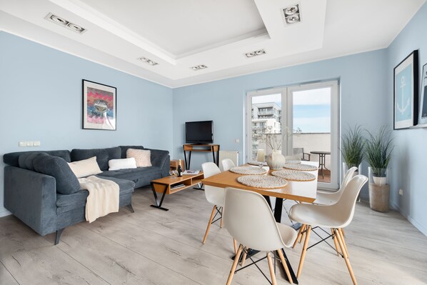 A modern living room with a sofa, dining table, chairs, and a TV. - Elite Apartments Marine Cztery Oceany (Gdansk)