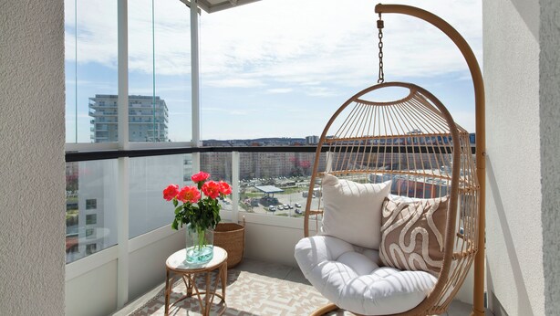 A balcony with a hanging chair, a small table with a vase of flowers, and a view of the cityscape. - Elite Apartments Marine Cztery Oceany (Gdansk)