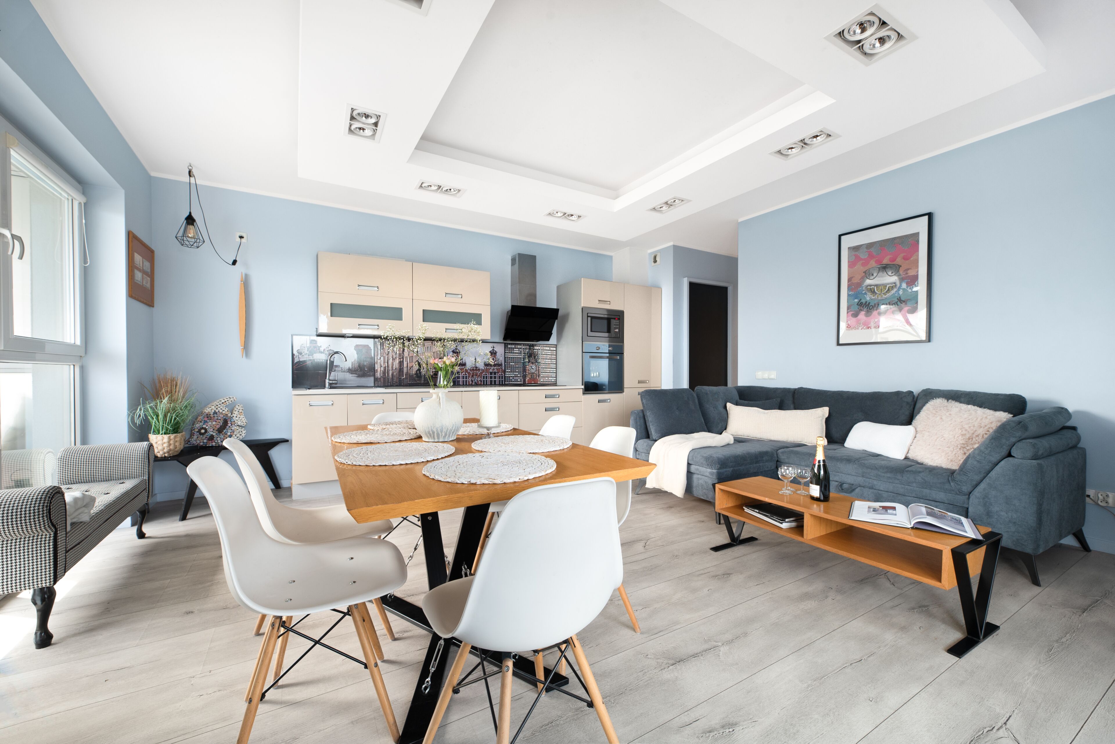 A modern living room with a dining area, a gray sofa, and a kitchen in the background.