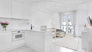 A modern, white-themed living space with a kitchen, a sofa, and a dining area. - Elite Apartments Marine Cztery Oceany (Gdansk)