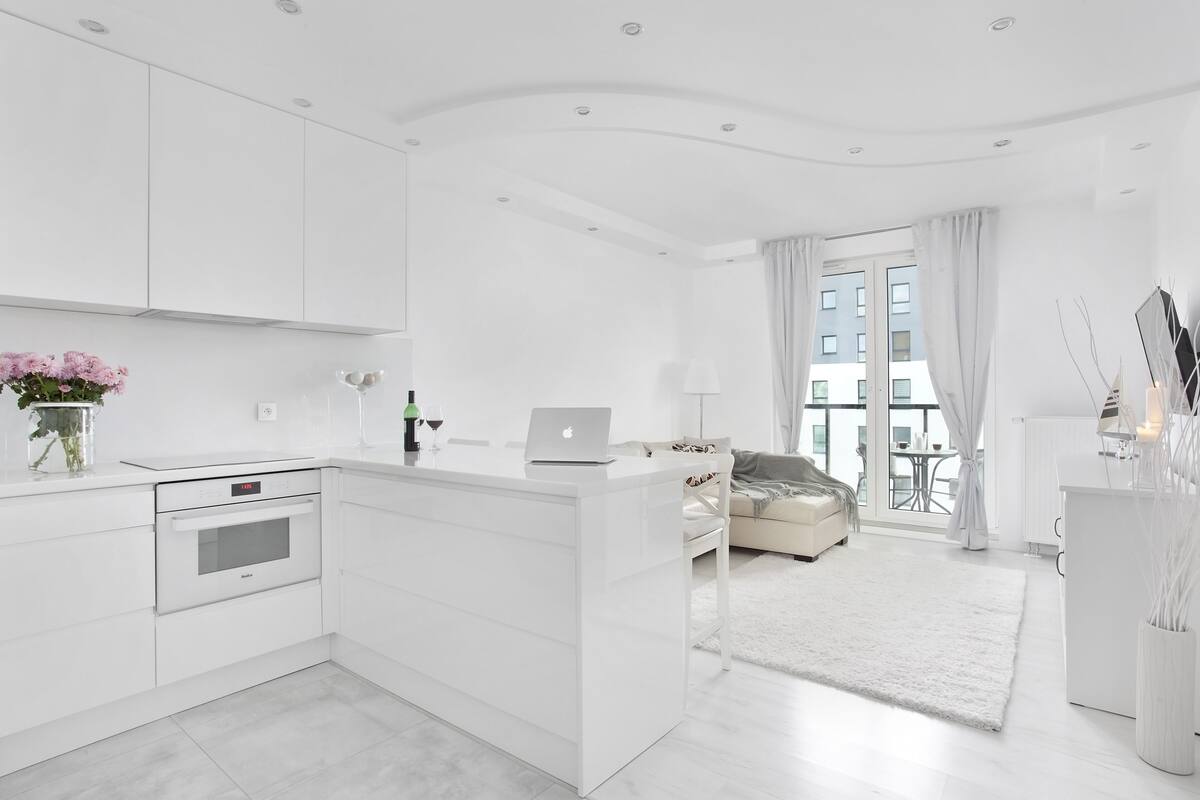 Un espace de vie moderne, aux tons clairs et blancs, comprenant une cuisine, un canapé et un coin repas.