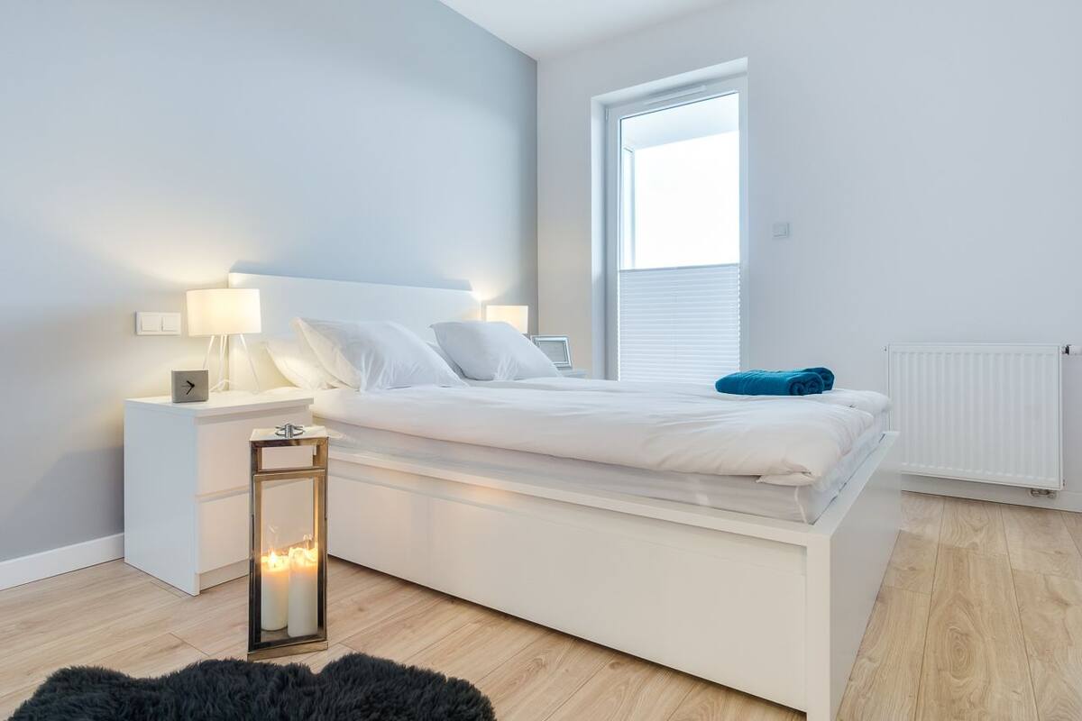 Une chambre à coucher moderne avec un lit blanc, des lampes de chevet, une table de chevet et une lampe sur pied.