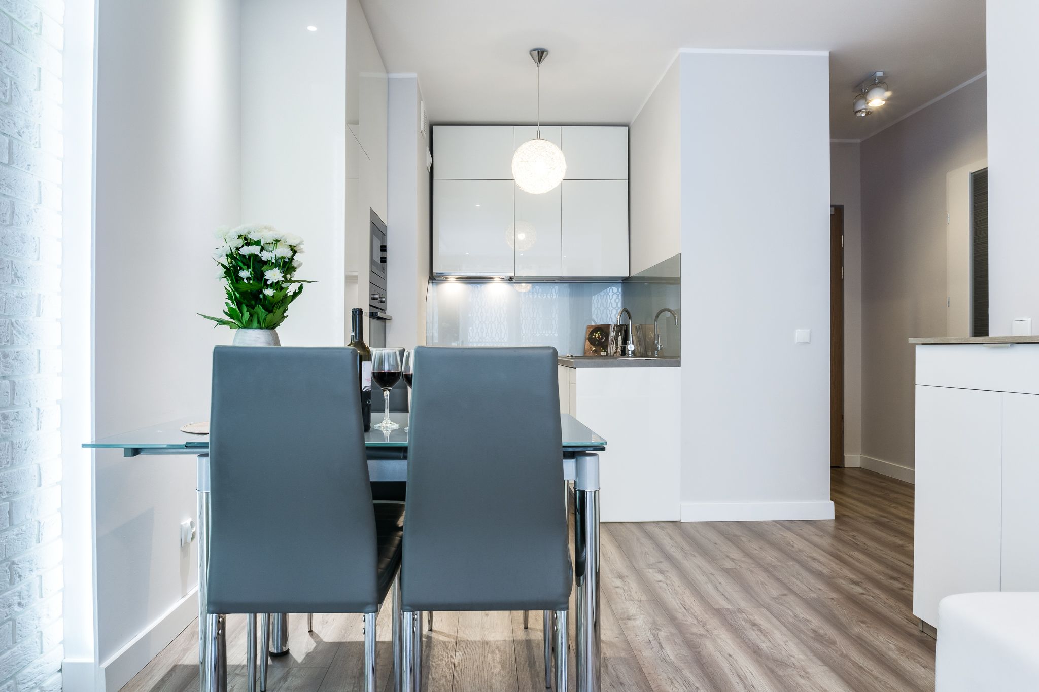 A modern kitchen with white cabinets, a hanging light fixture, and a dining area with a glass table and chairs.