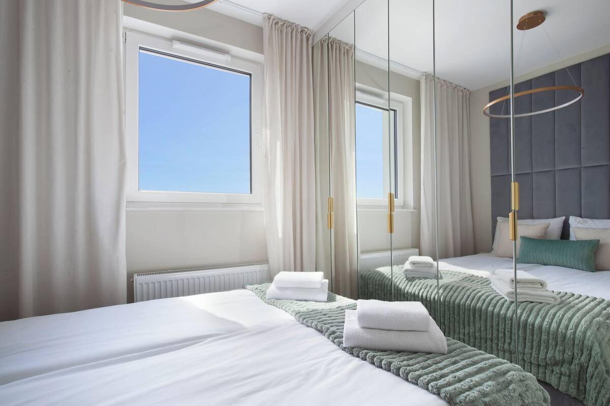 Une chambre d’hôtel avec deux lits, une grande fenêtre, un miroir et un luminaire suspendu moderne.