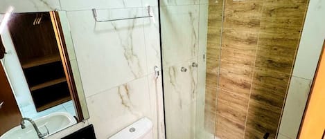 Un baño con lavamanos de mármol, inodoro y ducha con cerramiento de vidrio.