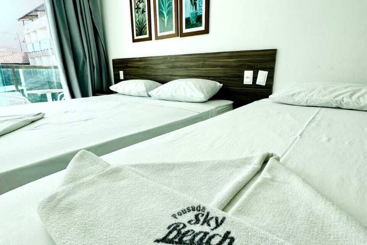 A hotel room with two beds, a large window with curtains, and three framed pictures on the wall.