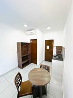 Una habitación pequeña y limpia con una mesa redonda de madera y dos sillas, un armario de madera, una puerta y una kitchenette con un fregadero y encimera.