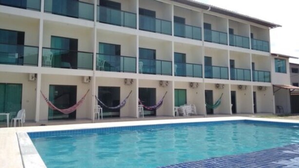 A hotel with a swimming pool, multiple balconies, and outdoor seating areas. - Pousada Sky Beach Flat (Ipojuca)