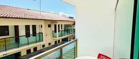 A balcony with a glass railing, a table, and red chairs.