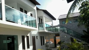 A modern two-story building with a glass balcony, a stone staircase, and a well-maintained garden with palm trees. - Pousada Sky Beach Flat (Ipojuca)