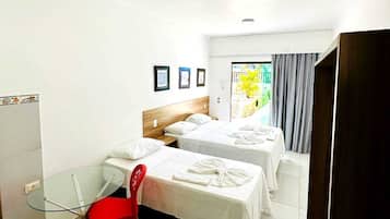 Quarto de hotel com duas camas, uma mesa de vidro, cadeiras vermelhas e vista para o exterior.