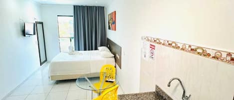 Une chambre d’hôtel de taille réduite, comprenant un lit, une petite kitchenette, une chaise jaune et une salle de bain.