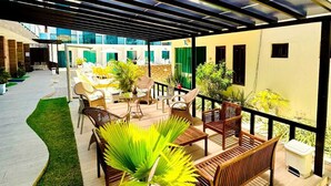 An outdoor patio area with seating, a small palm tree, and a covered walkway. - Pousada Sky Beach Flat (Ipojuca)