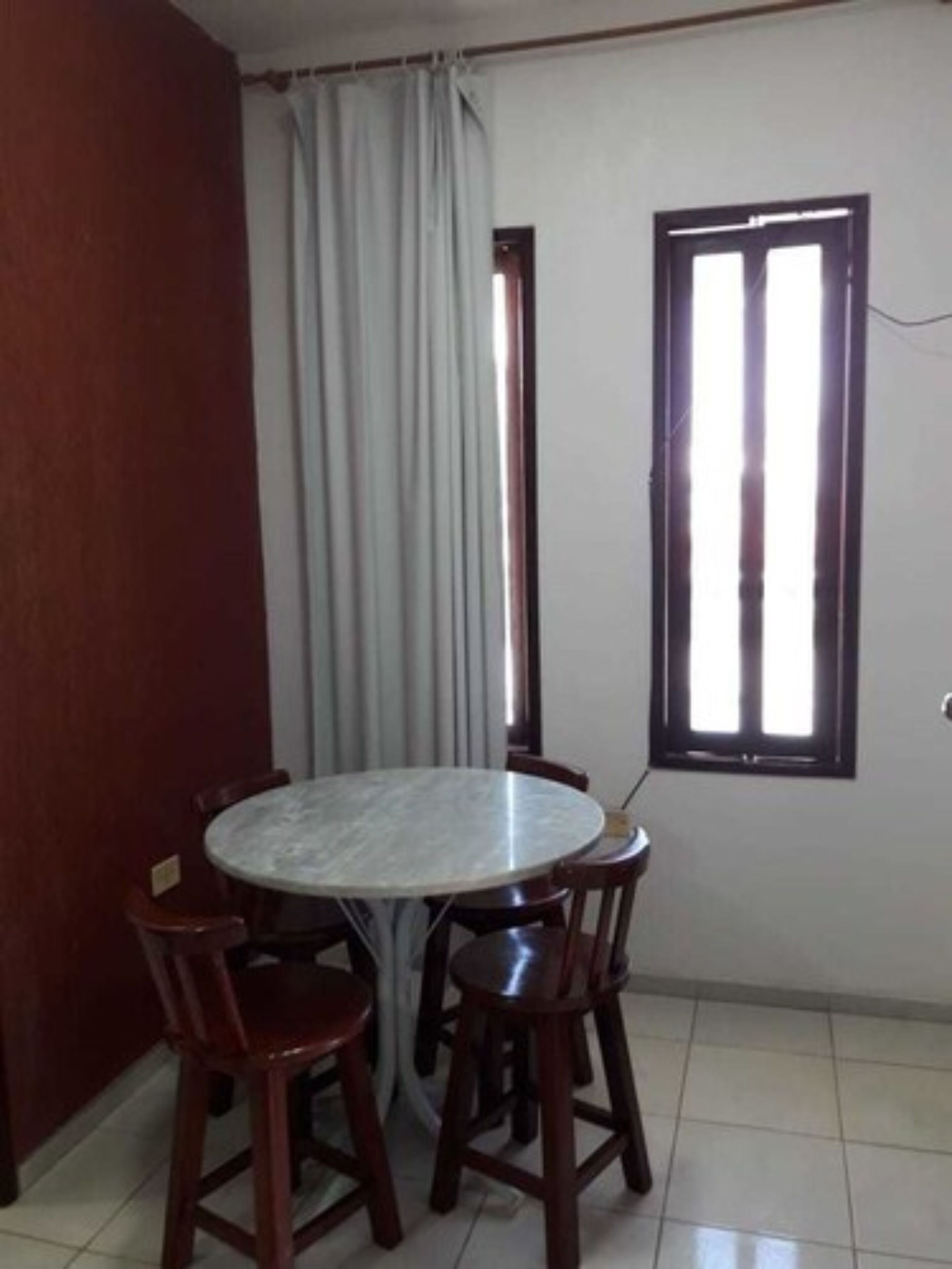 A dining area with a round table and four chairs, a window with blinds, and a curtain.