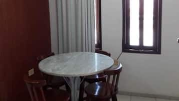 Un comedor con una mesa redonda y cuatro sillas, una ventana con persianas y una cortina.