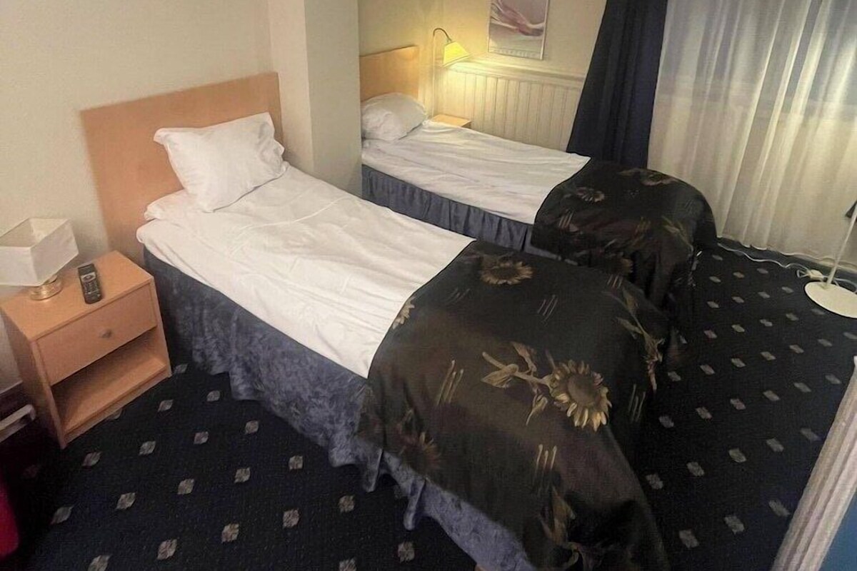 A hotel room with two beds, a nightstand, a lamp, and a mirror.