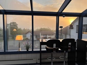 A room with a large window offering a view of houses and a mountain. There is a table with a lamp and a chair. - Welcome Inn Hotel Lyngskroa (Storfjord)