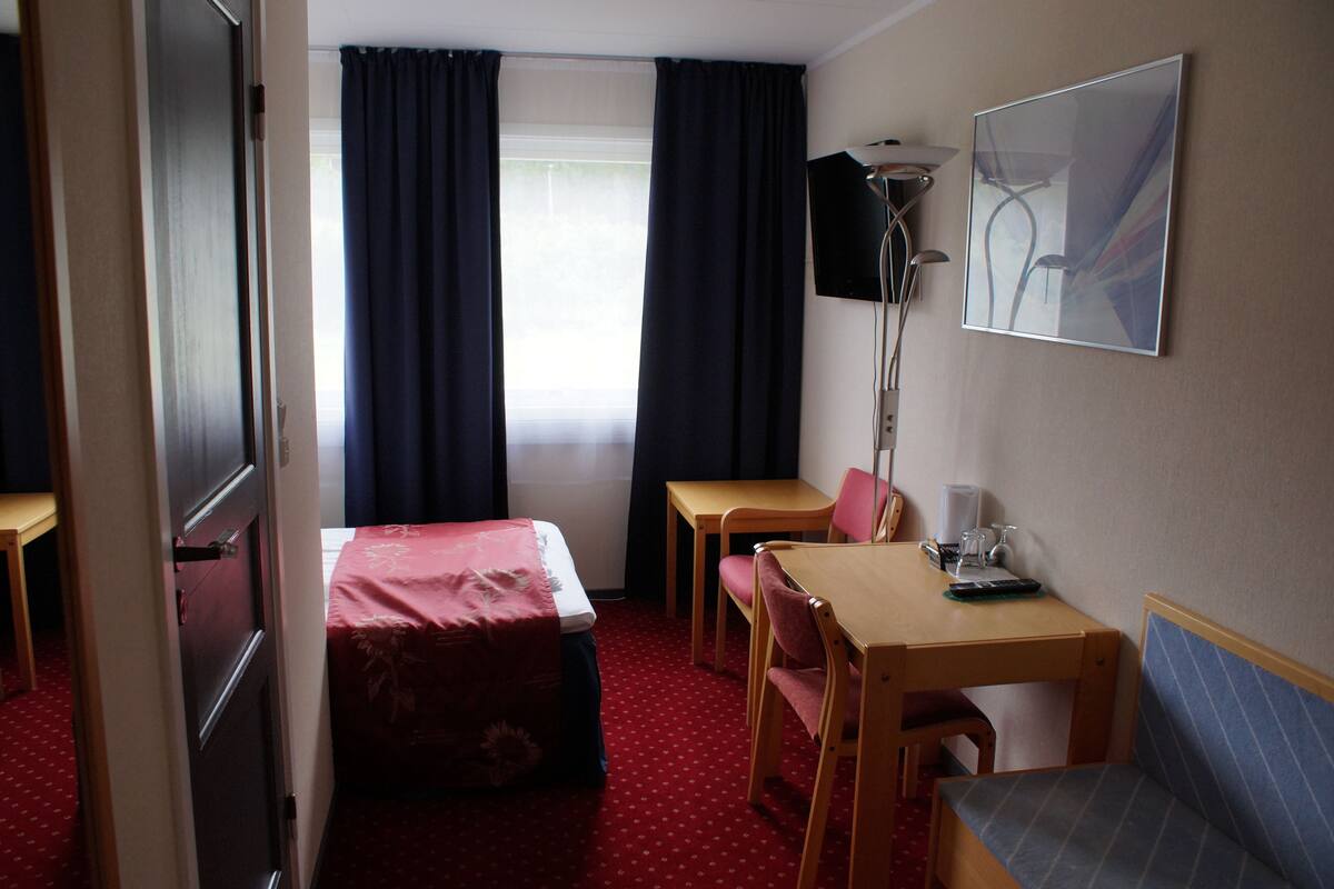 A hotel room with a bed, two chairs, a table, a desk, a lamp, and a painting on the wall.