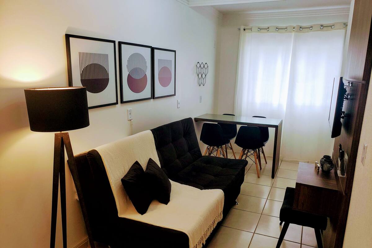 A living room with a black and white sofa, a small table, and a TV on a wooden stand.
