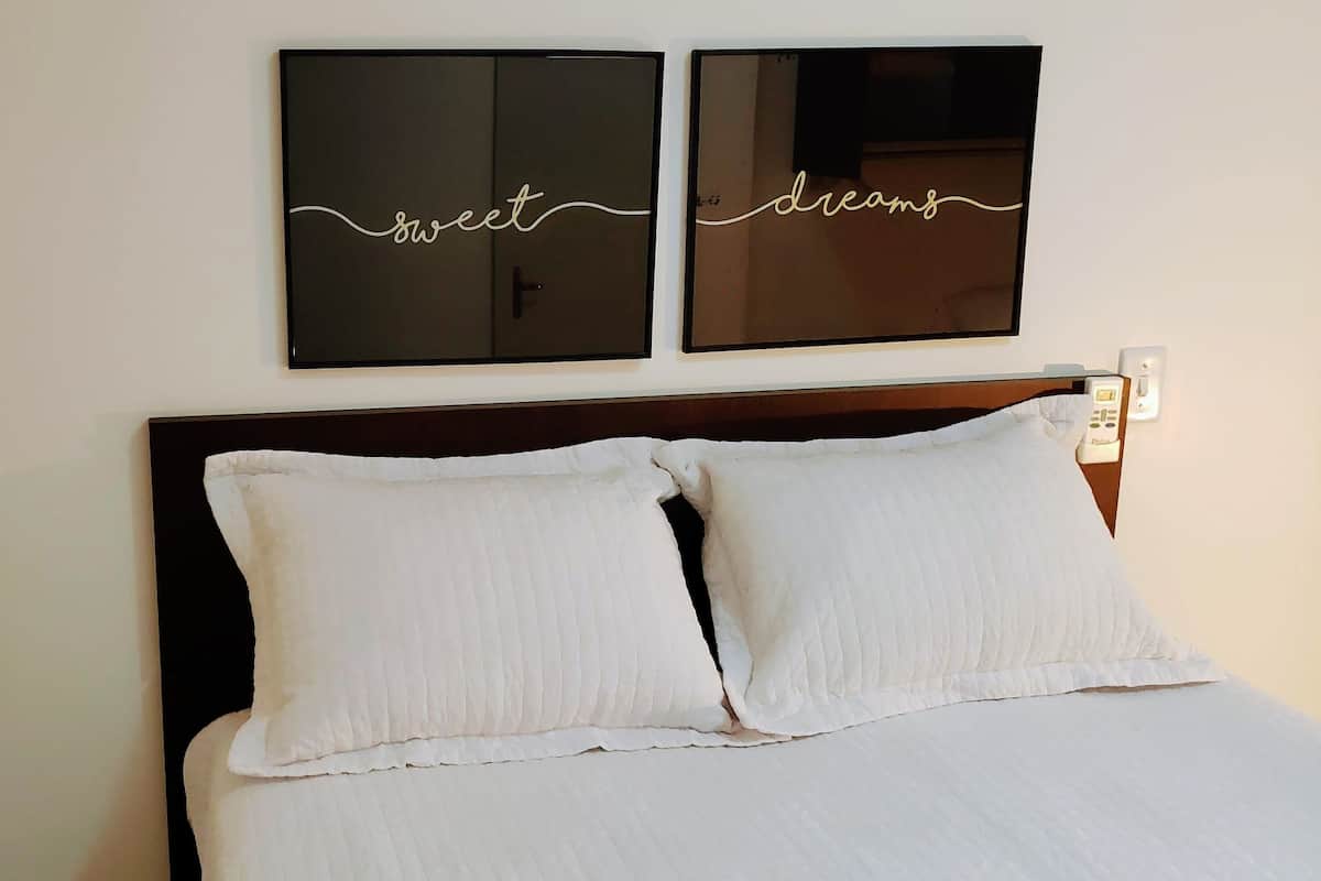 A bed with white linens and two pillows, a dark wooden headboard, and two framed signs on the wall with the words "sweet" and "dreams".