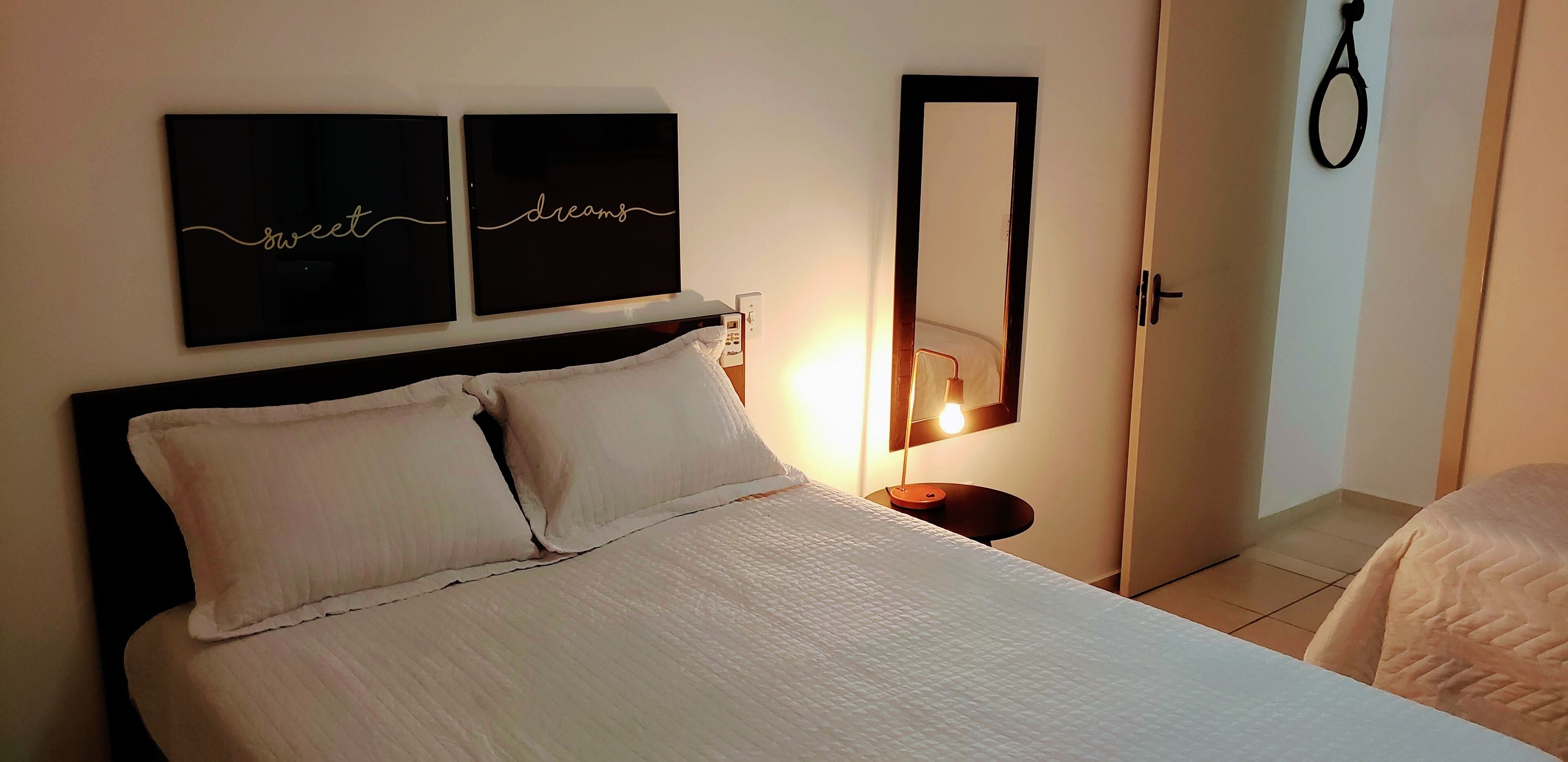 A neatly made bed with white bedding, a bedside table with a lamp, and two wall art pieces with the words "sweet" and "dreams".