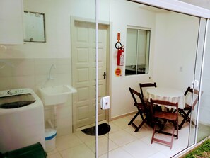 A small room with a washing machine, a sink, a door, a window, and a table with chairs.