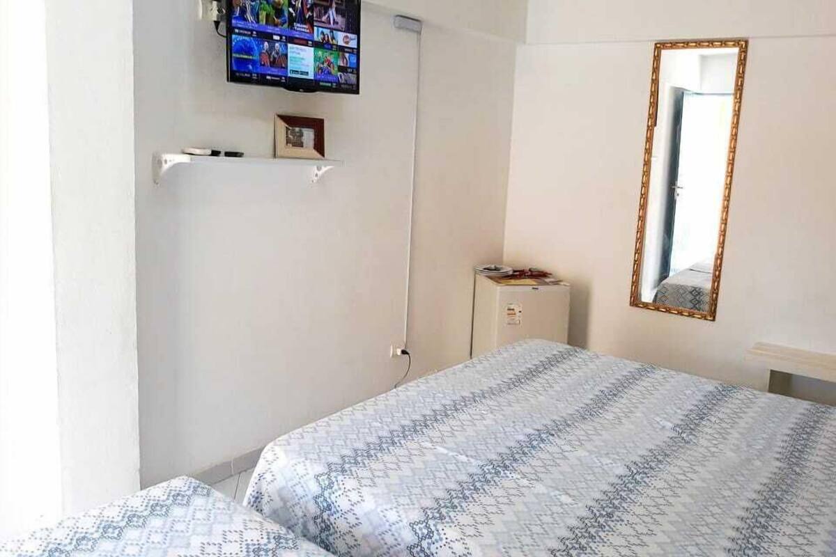 Quarto de hotel com uma cama, televisão na parede, um pequeno armário e um espelho.