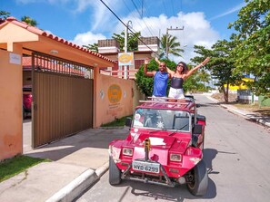 A red vehicle parked in front of a building with a closed gate and a sign with a phone number. - Pousada Santo Aleixo (Ipojuca)