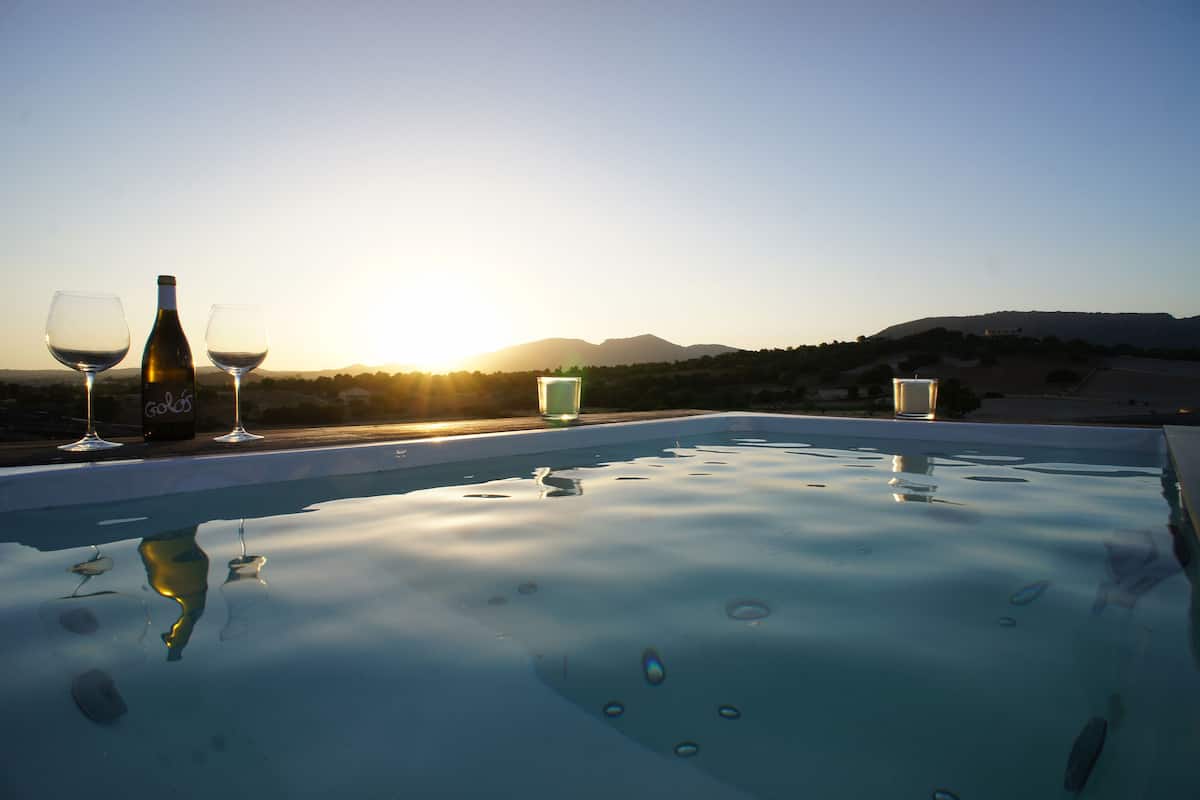 A pool with two wine glasses and a bottle, set against a sunset with mountains in the background.